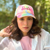 A woman wearing a multicolored tie-dye baseball cap with the 'Barbie' logo on it.