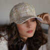 A woman wearing a beige tweed baseball cap with a pearl chain detail.