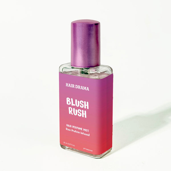 Pink bottle of 'Blush Rush' hair perfume mist with a purple cap on a white background