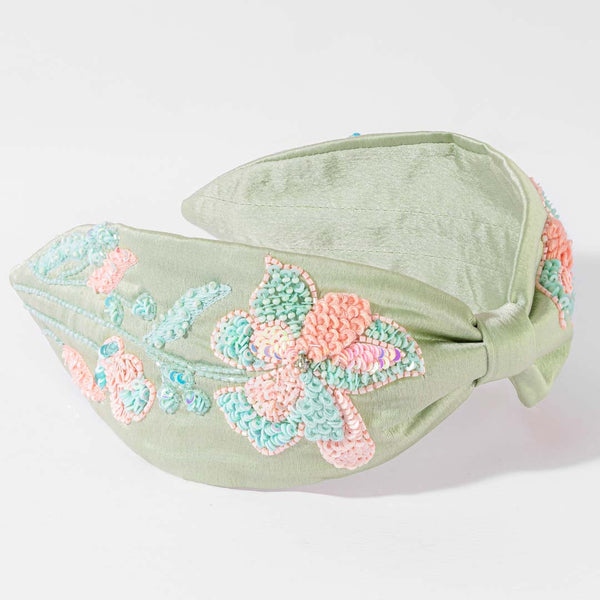 Green headband with floral embroidery on a light gray background