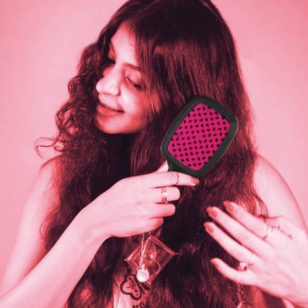 Woman brushing her hair with a pink and black brush against a pink background