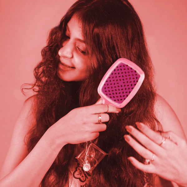 Woman brushing her hair with a pink brush against a pink background