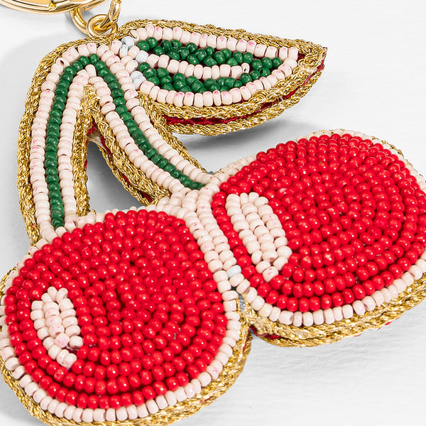 Beaded cherry keychain with red, green, and gold colors on a light background