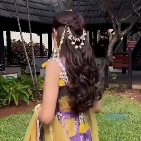 Woman in traditional attire with long hair and jewelry standing outdoors.