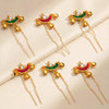 Set of six decorative hairpins with gold, red, and green colors on a beige background