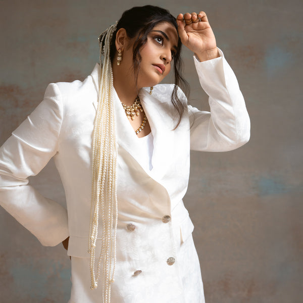 Woman in a white outfit with long pearl necklace against a neutral background