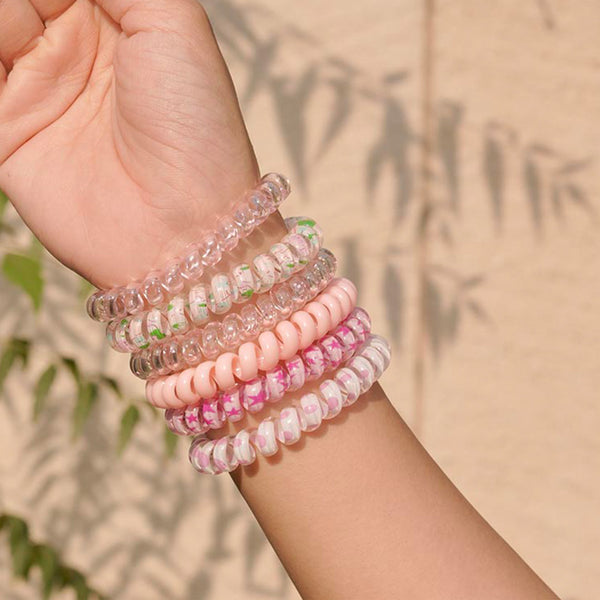 Hand wearing multiple beaded bracelets against a beige wall with greenery
