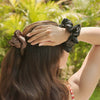 Person with hair tied back using scrunchies against a blurred green outdoor background