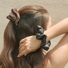 Person styling hair with a leopard print scrunchie and a gray scrunchie against a neutral background