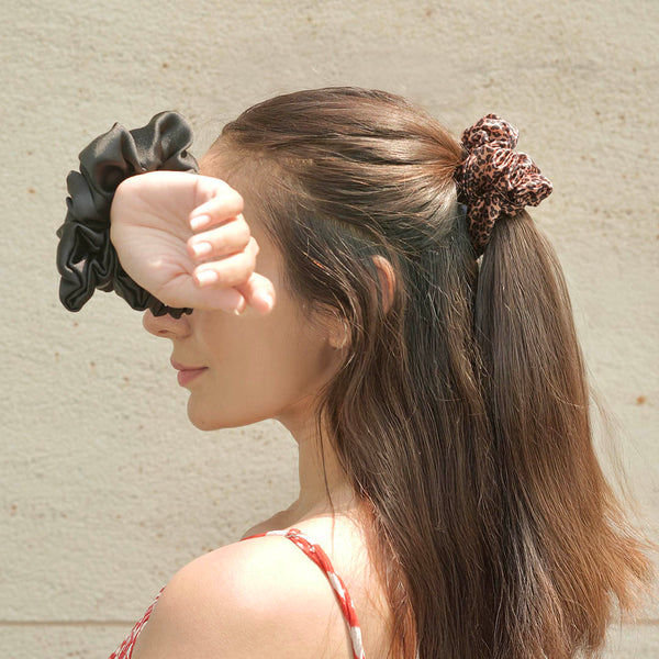 Woman with ponytail using scrunchies against a beige wall