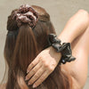 Person with leopard print scrunchie in hair and black scrunchie on wrist against a neutral background