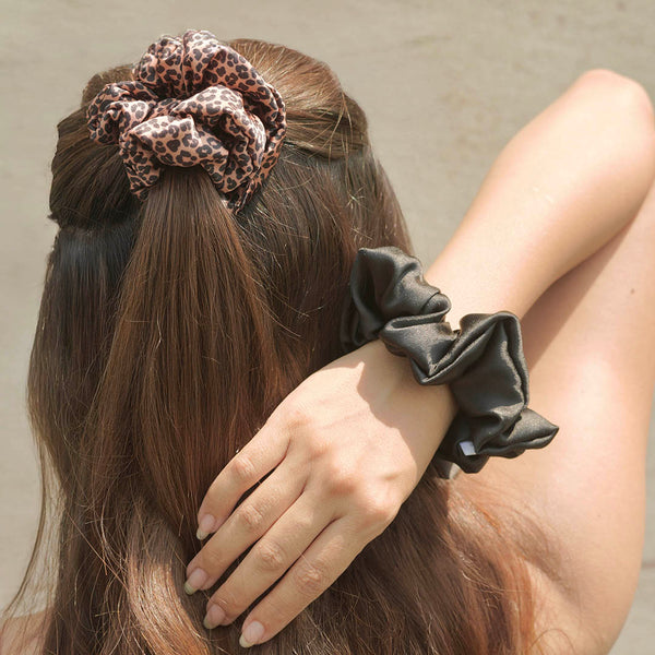 Person with leopard print scrunchie in hair and black scrunchie on wrist against a neutral background