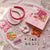 Hair accessories and DIY kit on a pink surface with flowers.