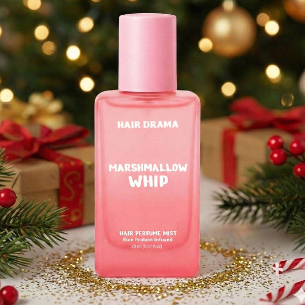 Pink bottle of 'Hair Drama Marshmallow Whip' hair perfume mist with Christmas decorations in the background