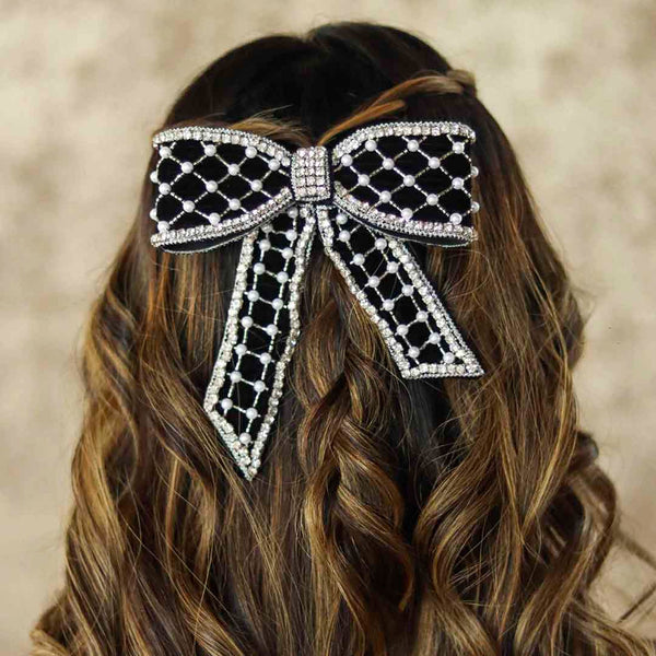 Black and silver bow hair accessory on wavy hair against a neutral background