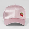 Pink satin baseball cap with cherry embellishment on a light gray background