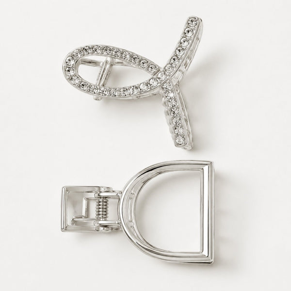 A silver-toned hair claw clip shown from two angles on a clean white background. One view shows the front with a curved open design set with clear rhinestones, and the other shows the back with a D-shaped frame and spring-loaded clasp mechanism.