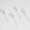 Set of five silver hairpins with floral designs on a light gray background