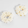 Pair of white floral earrings with gold and silver accents on a light gray background