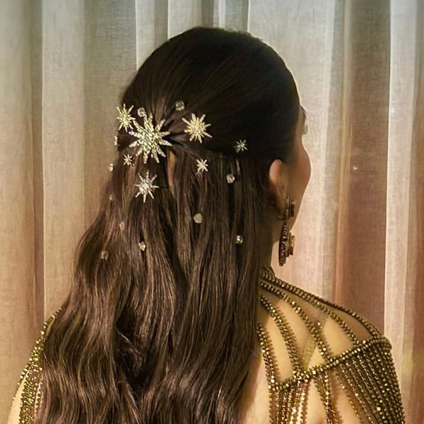 Woman with intricate hair styling and decorative hairpins against a neutral curtain background