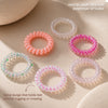 Set of colorful beaded hair ties on a textured beige surface with dried flowers.