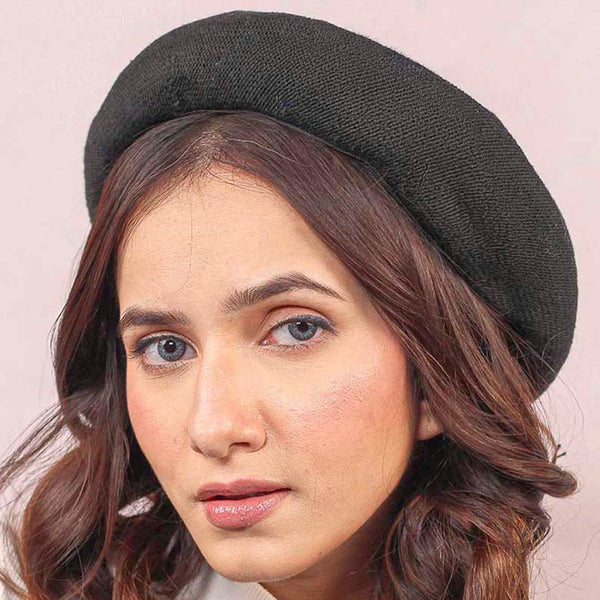 A woman wearing a black beret with a Eiffel Tower embellishment, paired with a white top.